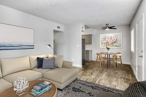 A living room with a beige couch, a coffee table, a ceiling fan, and a painting on the wall at Gilbert Square Apartments, Mesa, AZ 85203