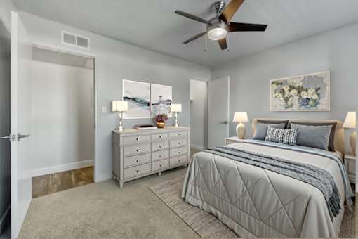 A bedroom with a large bed, a dresser, and a ceiling fan at Gilbert Square Apartments, Mesa, AZ