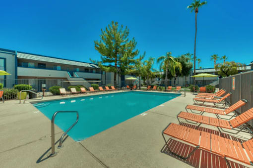 A pool surrounded by sun loungers and palm trees at Gilbert Square Apartments, Mesa, 85203