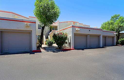 A tree is in front of a building with three garage doors.