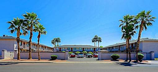Palm trees line the street in front of a white building.