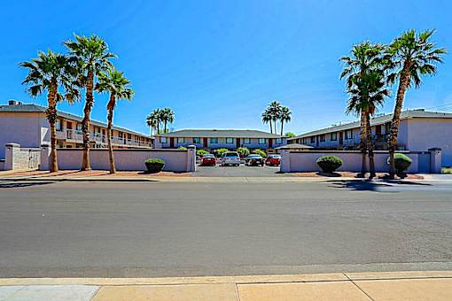 A parking lot with palm trees and a building in the background.