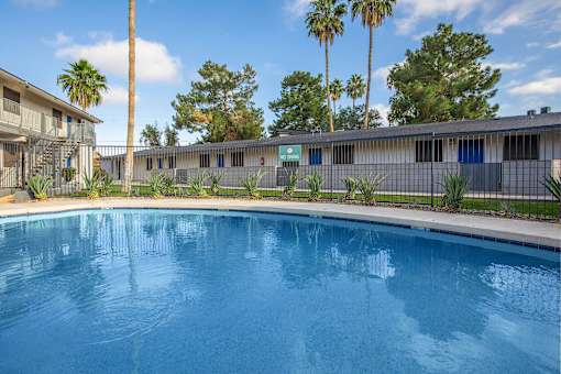 A swimming pool in front of a building with palm trees.