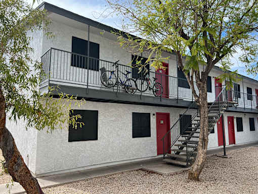 A white building with a red door and a bicycle hanging on the balcony.