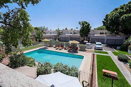 A pool surrounded by a fence and a patio with chairs.