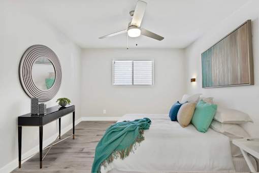 A bedroom with a bed, a mirror, a table, and a ceiling fan.