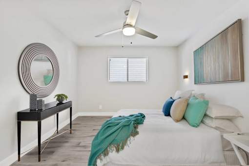 A bedroom with a bed, a mirror, a dresser, and a painting on the wall.