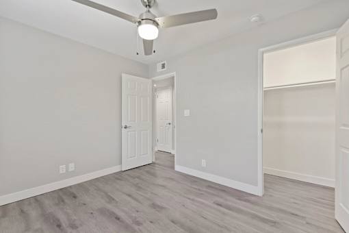 A room with a ceiling fan and light, two doors, and a window with blinds.