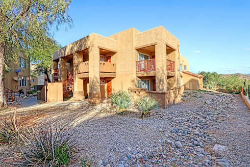 A building with a red balcony is surrounded by a gravel area and vegetation.
