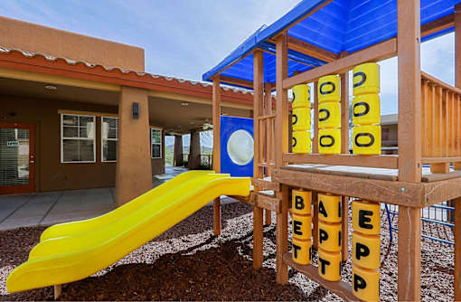 A playground with a yellow slide and a wooden structure with the word "BETTER" spelled out on it.