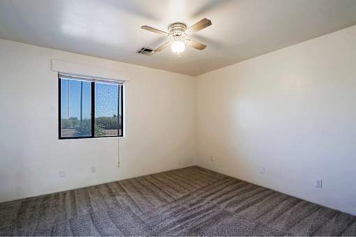 A room with a ceiling fan and a window overlooking a tree-lined street.