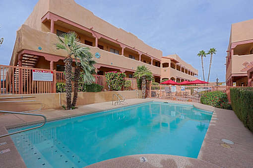 A large swimming pool in front of a building with a palm tree.