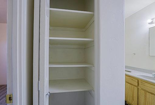 A white open closet with shelves and a mirror on the wall.