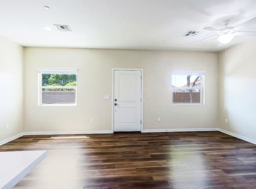 A room with a white door and two windows. The floor is hardwood and contrasts against the warm soft yellow walls.