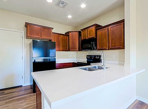 A kitchen with a black fridge and microwave, brown cabinets, and a white countertop.