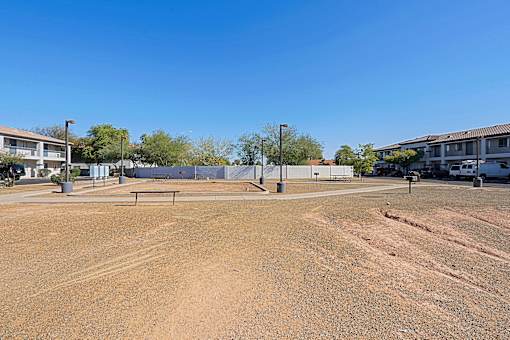 a dirt parking lot with houses on both sides and a bench