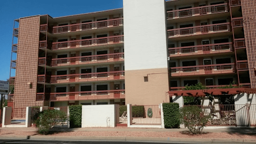 A large red brick building with balconies and a white door in front at Ambassador West Apartments, Phoenix