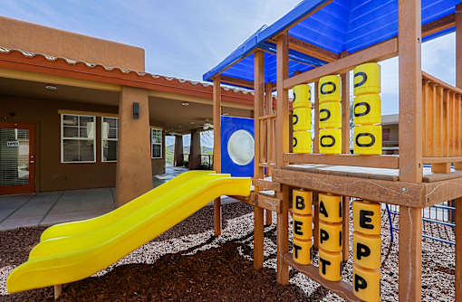 A playground with a yellow slide and a wooden structure with the word "BETTER" spelled out on it.