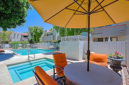 A yellow umbrella is over a table with chairs and a pool in the background.