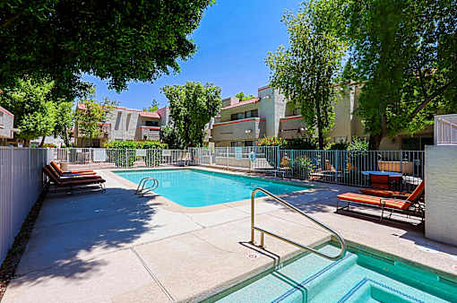 A pool surrounded by trees and chairs.