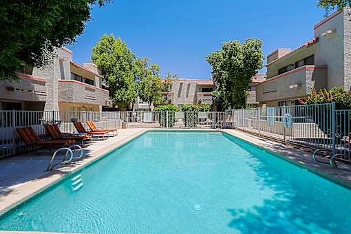 A swimming pool surrounded by chairs and trees.