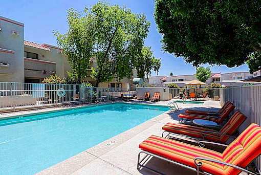 A pool surrounded by chairs and trees.
