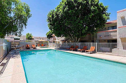 A swimming pool surrounded by trees and chairs.