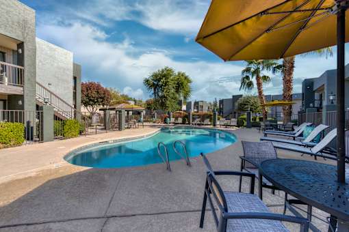 A pool area with a table and chairs and a yellow umbrella at Tela Verde Apartment Homes, Glendale, 85306