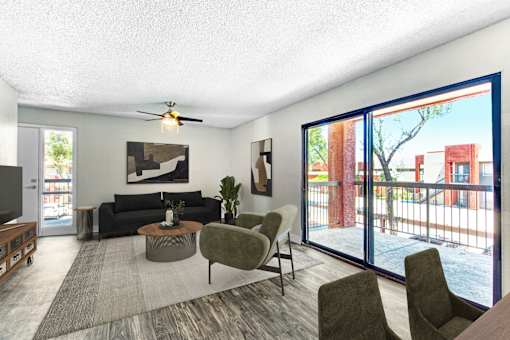 A living room with a black couch, a grey armchair, a coffee table, and a ceiling fan at Tela Verde Apartment Homes, Glendale, 85306