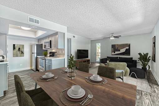 A dining table set with plates and cutlery is in the foreground of a modern kitchen and living room at Tela Verde Apartment Homes, Glendale, 85306