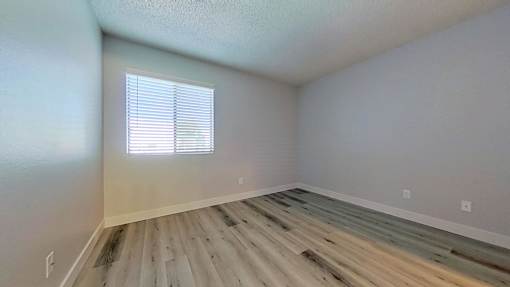 A room with wooden flooring and a window with blinds.