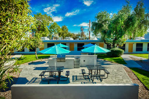 A patio with tables and chairs under blue umbrellas. at The Link Apartments, Mesa, Arizona