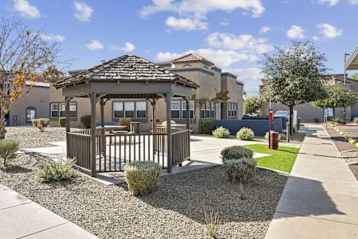 A gazebo is surrounded by a gravel bed in front of a building.
