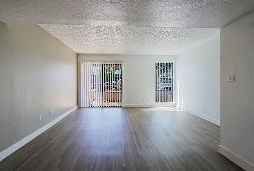 A spacious room with wooden floors and a view of a balcony through the windows.