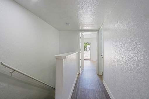 A long hallway with a white wall and a white door.