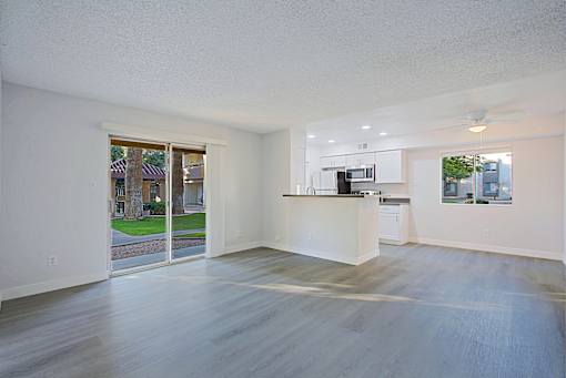 A spacious, empty room with a kitchen area visible through the glass door.