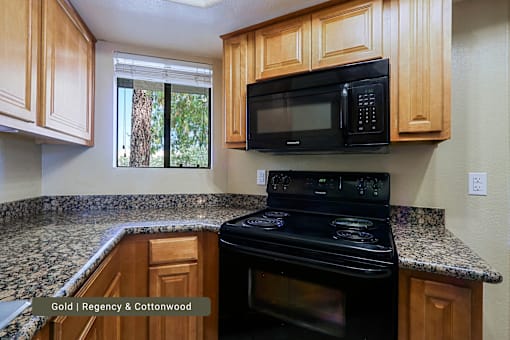 A black microwave is mounted above a black stove in a kitchen with wooden cabinets.