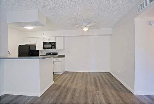 A kitchen with a black fridge and microwave, white cabinets, and a wooden floor.