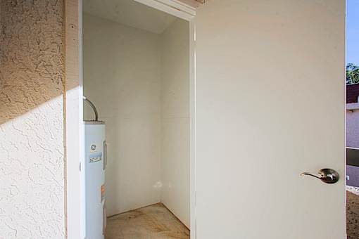 A white door with a silver handle is open to a room with a white wall and a white fridge.