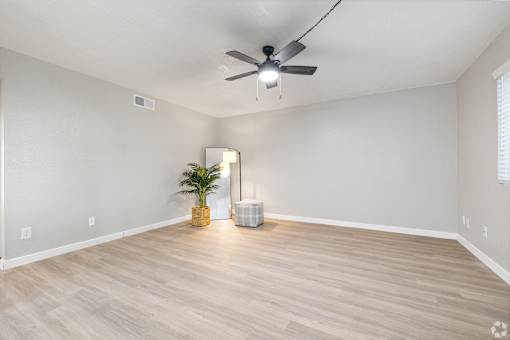 an empty living room with a ceiling fan and a plant