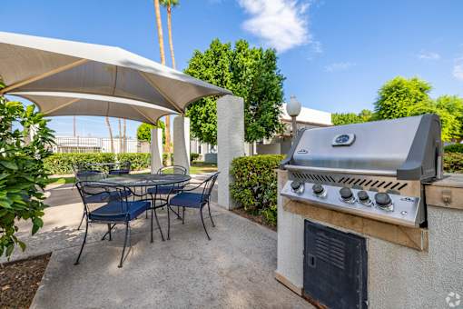 A patio with a grill and chairs under a white canopy.