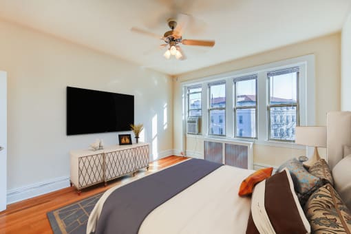 bedroom with bed, nightstand, tv, hardwood floors, ceiling fan and large windows at chatham courts apartments in washington dc