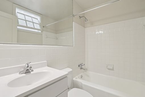 A white bathroom with a sink, tub, and window.