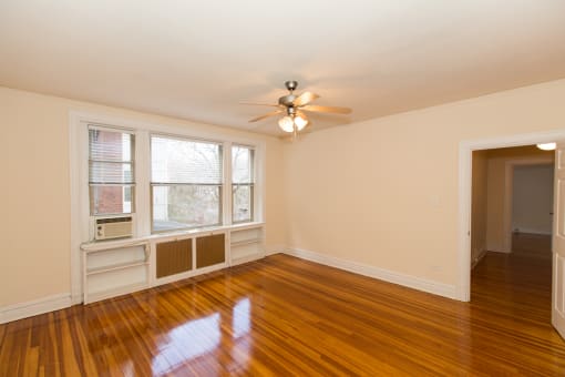 vacant living area with hardwood flooring, ceiling fan, and large windows at 2701 Connecticut apartments in washington dc