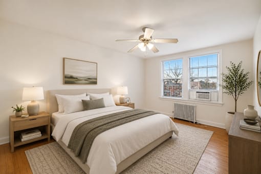 A bedroom with a large bed, a ceiling fan, and a window with a view of a cityscape.