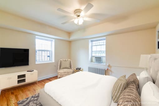 bedroom with bed, dresser, tv, seating area with windows and ceiling fan at 4031 davis place apartments in washington dc