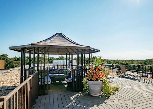 A gazebo with a table and chairs is surrounded by a deck and a railing.