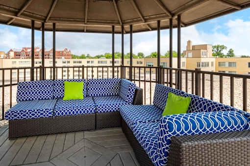 A blue and white patterned couch with green pillows sits on a wooden deck.
