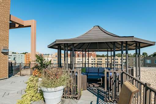 A gazebo with a metal roof is surrounded by potted plants and a metal fence.