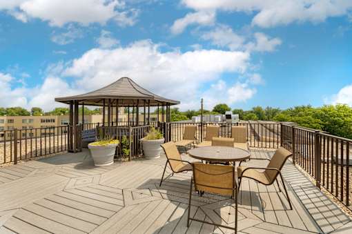 A gazebo is surrounded by chairs and tables on a wooden deck.